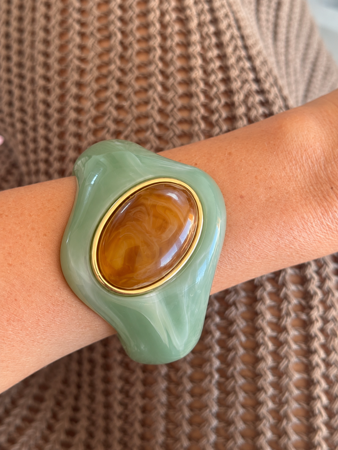 Brazalete escultórico verde menta con óvalo color ámbar sobre la muñeca