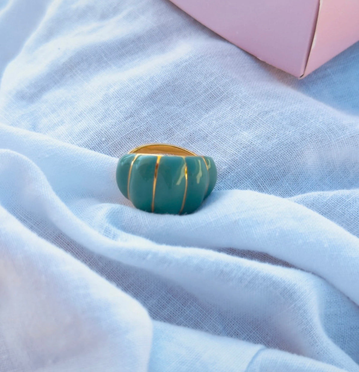 Anillo Rienzi verde menta con acabado dorado sobre tela blanca