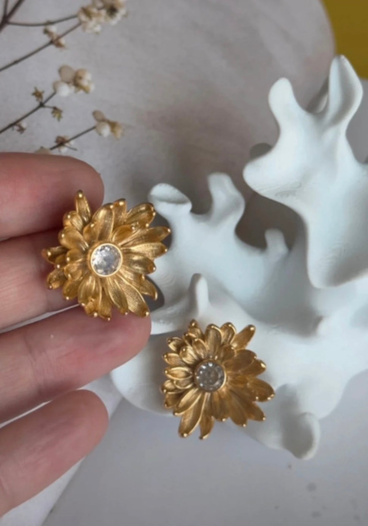 Detalle de pendiente Crisantemi dorado sostenido en la mano