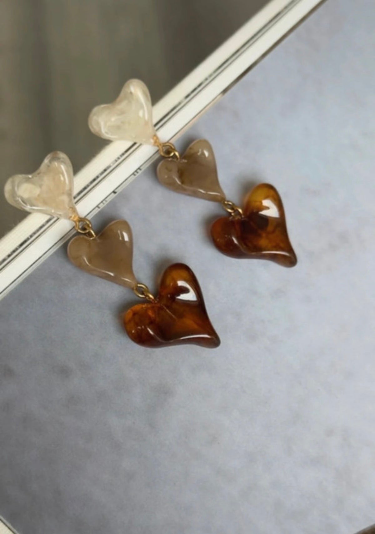 Pendientes largos de corazones marfil, miel y ámbar en composición editorial