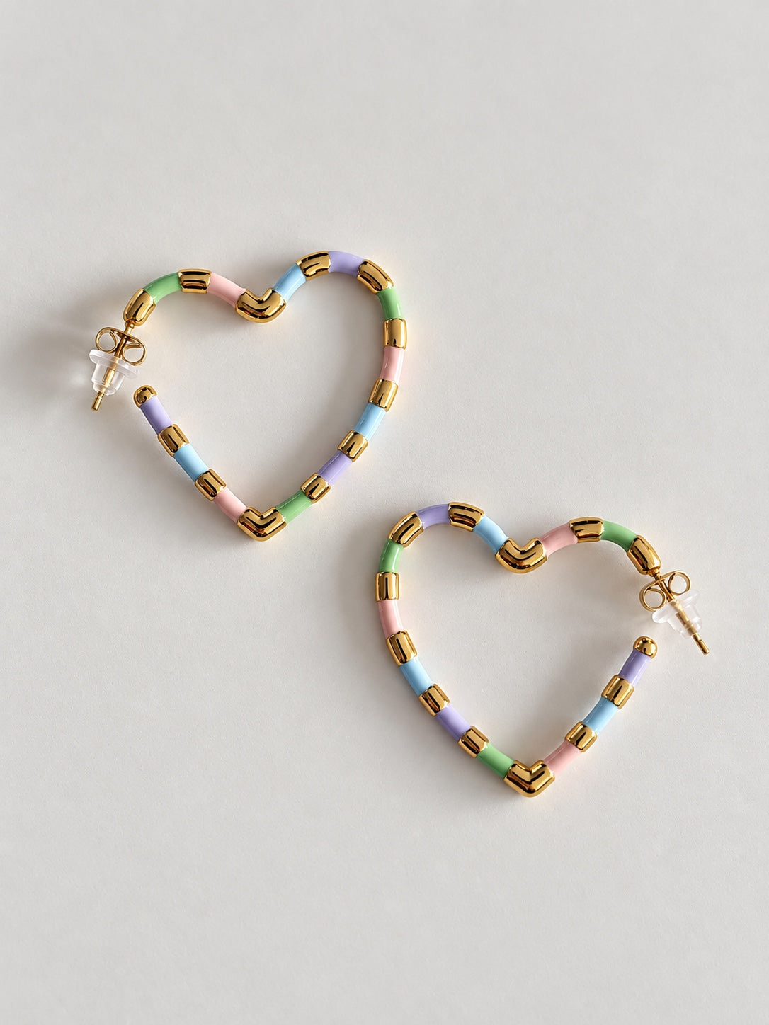Pendientes de corazón con detalles dorados y esmalte pastel sobre fondo claro