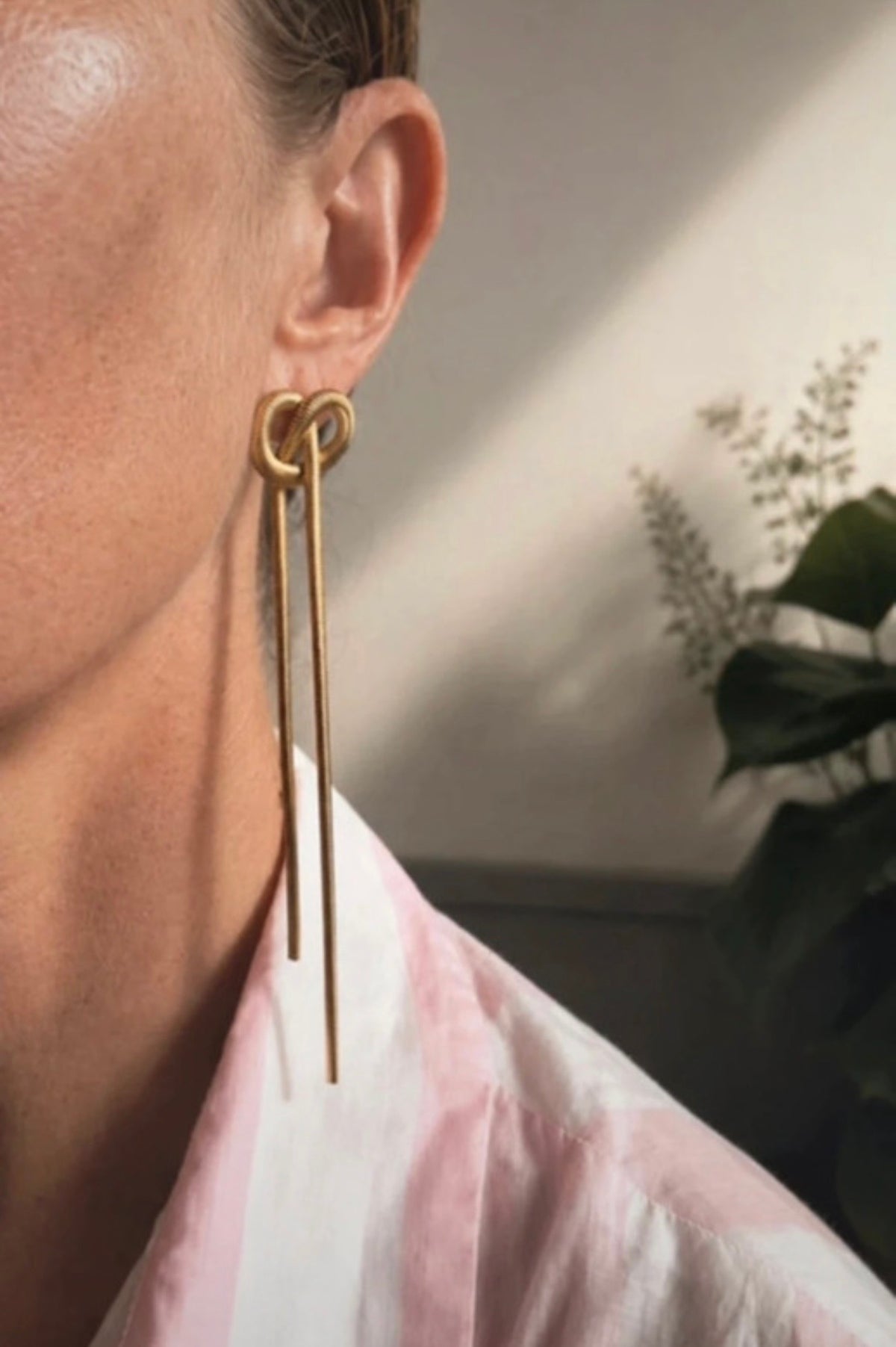 Pendientes Sospiri dorados sobre hojas verdes, detalle